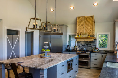 Example of a mid-sized trendy l-shaped medium tone wood floor and brown floor open concept kitchen design in Orlando with an undermount sink, shaker cabinets, gray cabinets, granite countertops, gray backsplash, stone tile backsplash, stainless steel appliances, an island and gray countertops