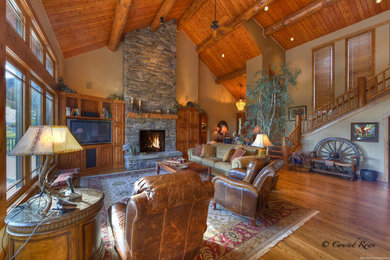 Cette image montre un salon chalet de taille moyenne et ouvert avec un mur beige, parquet foncé, une cheminée standard, un manteau de cheminée en pierre, un téléviseur encastré et un sol marron.