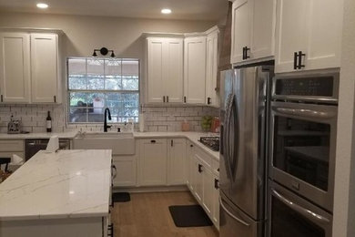 Medium tone wood floor and brown floor kitchen photo in Austin with a farmhouse sink, shaker cabinets, white cabinets, quartzite countertops, white backsplash, subway tile backsplash, stainless steel appliances, an island and white countertops