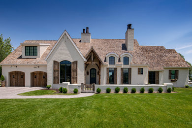 Large french country white two-story brick house exterior idea in Other with a gambrel roof, a shingle roof and a brown roof