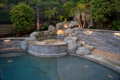 Photo of a large traditional backyard kidney-shaped pool in Los Angeles with a hot tub and natural stone pavers.
