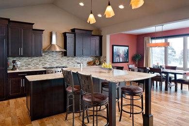 Eat-in kitchen - large modern l-shaped light wood floor eat-in kitchen idea in Omaha with recessed-panel cabinets, dark wood cabinets, beige backsplash, glass tile backsplash, stainless steel appliances, an island, granite countertops and a farmhouse sink