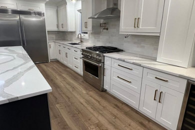 Photo of a mid-sized contemporary l-shaped eat-in kitchen in Toronto with an undermount sink, shaker cabinets, white cabinets, quartzite benchtops, grey splashback, ceramic splashback, stainless steel appliances, medium hardwood floors, with island, brown floor and white benchtop.