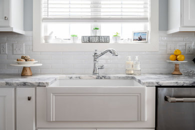 Foto på ett maritimt vit kök, med en undermonterad diskho, vita skåp, marmorbänkskiva, vitt stänkskydd, stänkskydd i tunnelbanekakel och rostfria vitvaror