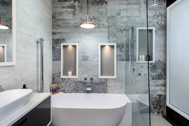 Small contemporary bathroom in Melbourne with black cabinets, a freestanding tub, an open shower, solid surface benchtops, a wall-mount toilet, porcelain tile, grey walls, a vessel sink, grey floor, an open shower, white benchtops, a niche, a single vanity, a floating vanity and vaulted.