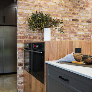 Zweizeilige, Geräumige Industrial Küche mit Vorratsschrank, Doppelwaschbecken, Schrankfronten im Shaker-Stil, grauen Schränken, Mineralwerkstoff-Arbeitsplatte, Küchenrückwand in Schwarz, Rückwand aus Metrofliesen, Küchengeräten aus Edelstahl, Betonboden, Kücheninsel, grauem Boden und weißer Arbeitsplatte in Sonstige