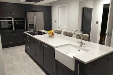 Medium sized contemporary kitchen/diner in Other with a belfast sink, shaker cabinets, grey cabinets, composite countertops, black appliances, vinyl flooring, an island, grey floors and grey worktops.