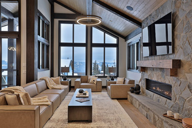 Example of a large mountain style open concept medium tone wood floor, brown floor and vaulted ceiling living room design in Vancouver with white walls, a standard fireplace, a wall-mounted tv and a stone fireplace