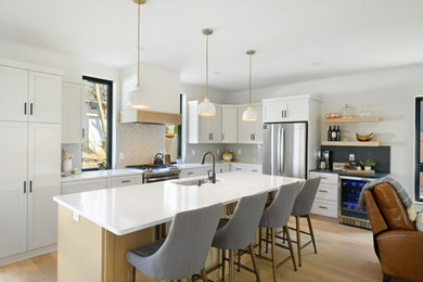 Kitchen - mid-sized l-shaped medium tone wood floor and brown floor kitchen idea in Minneapolis with an undermount sink, shaker cabinets, white cabinets, quartz countertops, white backsplash, ceramic backsplash, stainless steel appliances, an island and white countertops