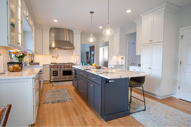 Transitional light wood floor eat-in kitchen photo in Baltimore with a farmhouse sink, recessed-panel cabinets, white cabinets, marble countertops, white backsplash, subway tile backsplash, stainless steel appliances, an island and white countertops