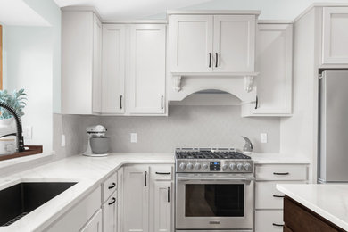 Example of a mid-sized transitional l-shaped light wood floor and beige floor kitchen design in Minneapolis with an undermount sink, shaker cabinets, white cabinets, quartz countertops, white backsplash, ceramic backsplash, stainless steel appliances, an island and white countertops