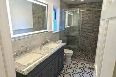 Inspiration for a mid-sized contemporary gray tile and ceramic tile ceramic tile, white floor and double-sink alcove shower remodel in New York with raised-panel cabinets, gray cabinets, a one-piece toilet, white walls, marble countertops, gray countertops and a freestanding vanity