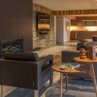 Exemple d'un très grand sous-sol rétro donnant sur l'extérieur avec un mur gris, un sol en carrelage de porcelaine, une cheminée standard, un manteau de cheminée en carrelage et un sol gris.