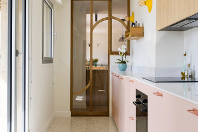 Modelo de cocina lineal contemporánea de tamaño medio cerrada con puertas de armarios rosa, encimera de cuarcita, salpicadero blanco, puertas de cuarzo sintético, electrodomésticos negros, suelo de terrazo, suelo multicolor y encimeras blancas