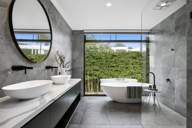 This is an example of a large contemporary kids bathroom in Melbourne with flat-panel cabinets, black cabinets, a freestanding tub, an open shower, gray tile, ceramic tile, grey walls, ceramic floors, a vessel sink, engineered quartz benchtops, grey floor, an open shower, white benchtops, a double vanity and a floating vanity.