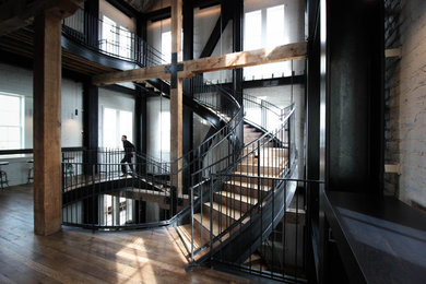 Example of a huge urban wooden spiral metal railing and brick wall staircase design in Other with wooden risers
