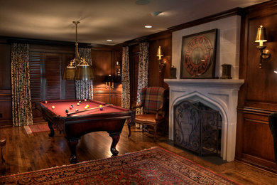 Modelo de sala de juegos en casa abierta clásica grande con paredes rojas, suelo de madera en tonos medios, todas las chimeneas y marco de chimenea de piedra