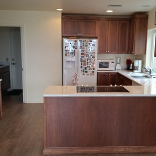 Aménagement d'une grande arrière-cuisine moderne avec un évier encastré, un placard à porte shaker, des portes de placard en bois brun, un plan de travail en verre, une crédence blanche, un électroménager blanc, un sol en bois brun et une péninsule.