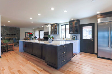 This is an example of an expansive modern single-wall open plan kitchen in Albuquerque with a farmhouse sink, shaker cabinets, dark wood cabinets, quartz benchtops, yellow splashback, ceramic splashback, stainless steel appliances, light hardwood floors, with island, beige floor and white benchtop.