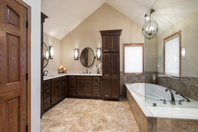 Example of a large classic master brown tile and stone tile travertine floor and brown floor bathroom design in Cleveland with recessed-panel cabinets, dark wood cabinets, beige walls, an undermount sink, a hinged shower door and beige countertops