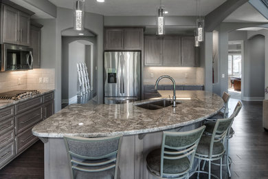 Inspiration for a contemporary dark wood floor and brown floor kitchen remodel in Omaha with an undermount sink, flat-panel cabinets, gray cabinets, granite countertops, white backsplash, porcelain backsplash, stainless steel appliances and an island