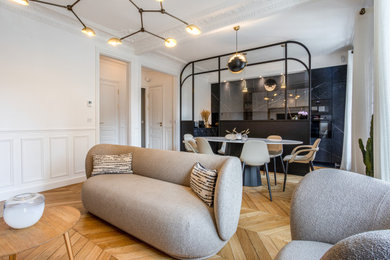 Diseño de sala de estar con barra de bar abierta contemporánea de tamaño medio sin chimenea con paredes blancas, suelo de madera clara, televisor colgado en la pared, suelo marrón y boiserie