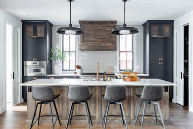 Example of a mid-sized transitional medium tone wood floor and brown floor kitchen design in Denver with a farmhouse sink, shaker cabinets, blue cabinets, quartzite countertops, beige backsplash, paneled appliances, an island and beige countertops