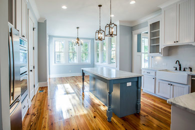 Eat-in kitchen - mid-sized cottage u-shaped light wood floor eat-in kitchen idea in Charleston with a farmhouse sink, white cabinets, white backsplash, subway tile backsplash, black appliances and an island