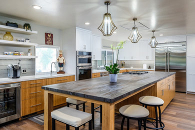 Large midcentury l-shaped eat-in kitchen in Sacramento with a farmhouse sink, flat-panel cabinets, medium wood cabinets, quartz benchtops, grey splashback, ceramic splashback, stainless steel appliances, medium hardwood floors, with island, brown floor and brown benchtop.