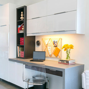 This is an example of a small modern study in San Diego with concrete flooring, a built-in desk and white walls.