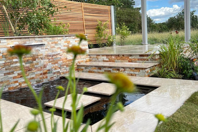 Design ideas for a small contemporary back xeriscape full sun garden for summer in Cambridgeshire with a pond, natural stone paving and a wood fence.