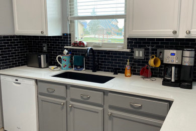 Inspiration for a mid-sized farmhouse l-shaped vinyl floor and gray floor eat-in kitchen remodel in Denver with a farmhouse sink, raised-panel cabinets, white cabinets, solid surface countertops, black backsplash, porcelain backsplash, white appliances, no island and white countertops