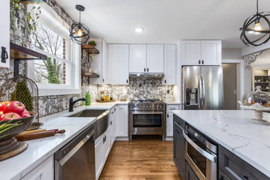 Large elegant l-shaped medium tone wood floor and brown floor open concept kitchen photo in Wilmington with a farmhouse sink, recessed-panel cabinets, white cabinets, quartz countertops, multicolored backsplash, ceramic backsplash, stainless steel appliances, an island and white countertops