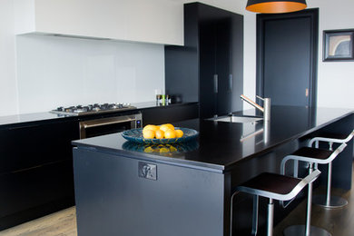 This is an example of a contemporary kitchen in Auckland with a single-bowl sink, black cabinets, white splashback, glass sheet splashback, stainless steel appliances, medium hardwood floors and with island.