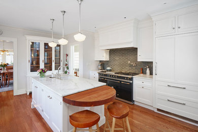 Large elegant u-shaped medium tone wood floor enclosed kitchen photo in Chicago with a farmhouse sink, beaded inset cabinets, white cabinets, marble countertops, green backsplash, ceramic backsplash, black appliances and an island