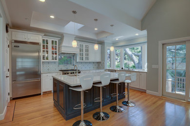 This is an example of a large traditional l-shaped kitchen in San Francisco with an undermount sink, raised-panel cabinets, white cabinets, solid surface benchtops, blue splashback, cement tile splashback, stainless steel appliances, medium hardwood floors, with island and brown floor.