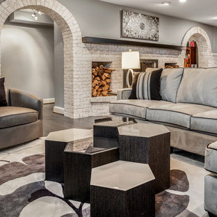 This is an example of a medium sized modern walk-out basement in DC Metro with grey walls, medium hardwood flooring, a standard fireplace, a brick fireplace surround and brown floors.