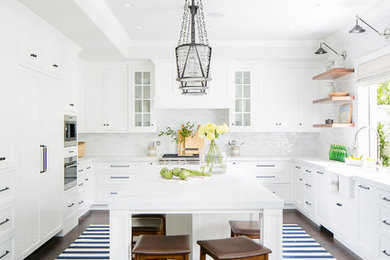 Eat-in kitchen - coastal u-shaped dark wood floor and brown floor eat-in kitchen idea in Orange County with a farmhouse sink, recessed-panel cabinets, white cabinets, white backsplash, stainless steel appliances, an island and white countertops