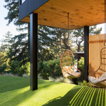Sheltered outdoor living area beneath ADU wing with hanging rattan chairs