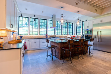 Photo of an expansive country u-shaped eat-in kitchen in Philadelphia with an undermount sink, shaker cabinets, white cabinets, soapstone benchtops, white splashback, subway tile splashback, stainless steel appliances, porcelain floors, with island, grey floor and black benchtop.