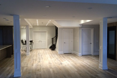 Large transitional underground light wood floor and beige floor basement photo in Toronto with gray walls