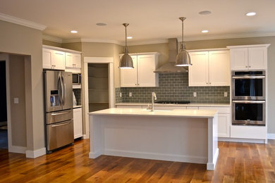 Mid-sized transitional l-shaped medium tone wood floor and brown floor open concept kitchen photo in Providence with a farmhouse sink, shaker cabinets, white cabinets, quartzite countertops, gray backsplash, subway tile backsplash, stainless steel appliances and an island