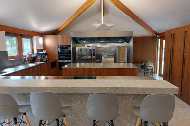 Bild på ett stort funkis grå grått kök, med en integrerad diskho, släta luckor, skåp i slitet trä, bänkskiva i rostfritt stål, stänkskydd med metallisk yta, svarta vitvaror, klinkergolv i keramik, en köksö och grått golv