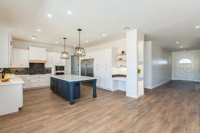 Photo of a large arts and crafts u-shaped open plan kitchen in Phoenix with recessed-panel cabinets, white cabinets, black splashback, subway tile splashback, stainless steel appliances, medium hardwood floors, with island, brown floor, white benchtop and solid surface benchtops.