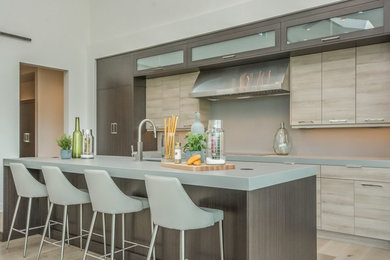 Example of a mid-sized trendy galley light wood floor and beige floor open concept kitchen design in Other with an undermount sink, flat-panel cabinets, light wood cabinets, quartz countertops, paneled appliances and an island