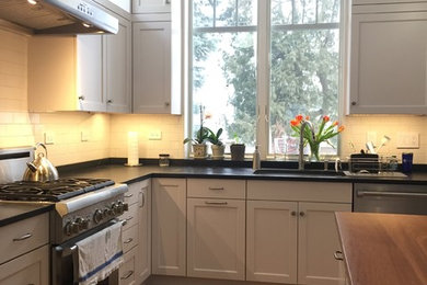 Eat-in kitchen - mid-sized transitional l-shaped medium tone wood floor and brown floor eat-in kitchen idea in Boston with an undermount sink, shaker cabinets, white cabinets, soapstone countertops, white backsplash, ceramic backsplash, stainless steel appliances, an island and gray countertops