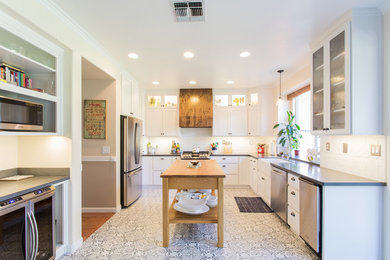 Large country u-shaped eat-in kitchen in San Francisco with a farmhouse sink, white cabinets, solid surface benchtops, white splashback, stainless steel appliances, ceramic floors, with island and grey benchtop.