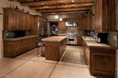 Open concept kitchen - large southwestern l-shaped ceramic tile open concept kitchen idea in Phoenix with a drop-in sink, raised-panel cabinets, brown cabinets, granite countertops, beige backsplash, ceramic backsplash, stainless steel appliances and an island