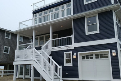 Large beach style blue three-story vinyl and clapboard exterior home photo in New York with a shingle roof and a black roof