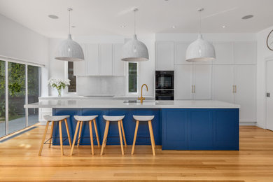Photo of a large galley kitchen/diner in Melbourne with a submerged sink, shaker cabinets, blue cabinets, engineered stone countertops, engineered quartz splashback, black appliances, medium hardwood flooring, an island and white worktops.